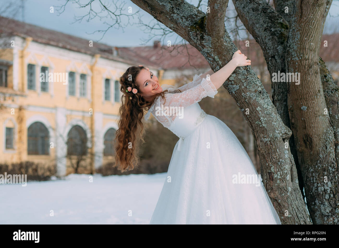 Smiling bride avec des roses dans les cheveux près de l'arbre Banque D'Images
