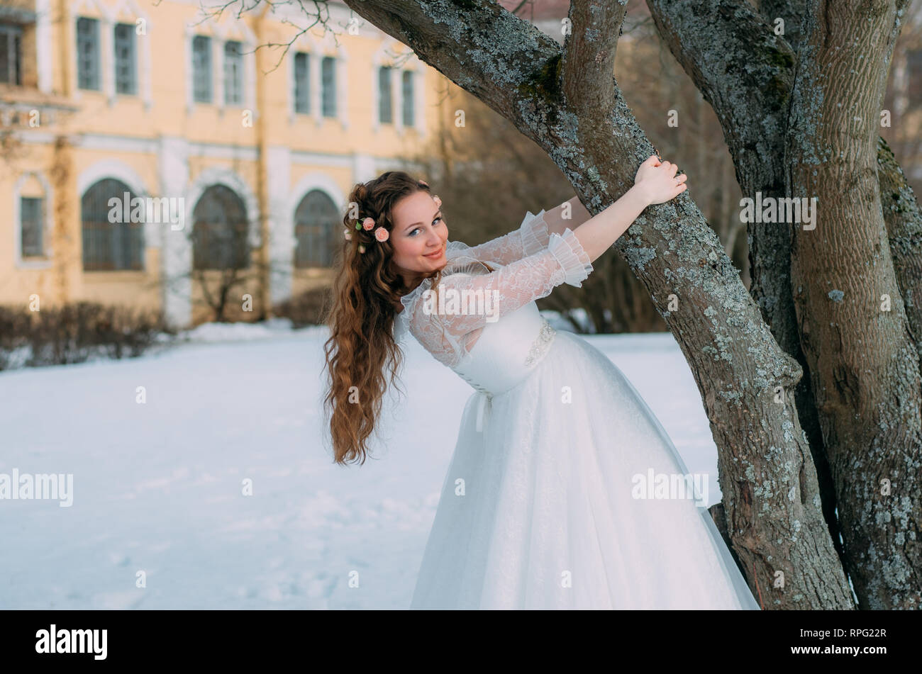 Smiling bride avec des roses dans les cheveux près de l'arbre Banque D'Images