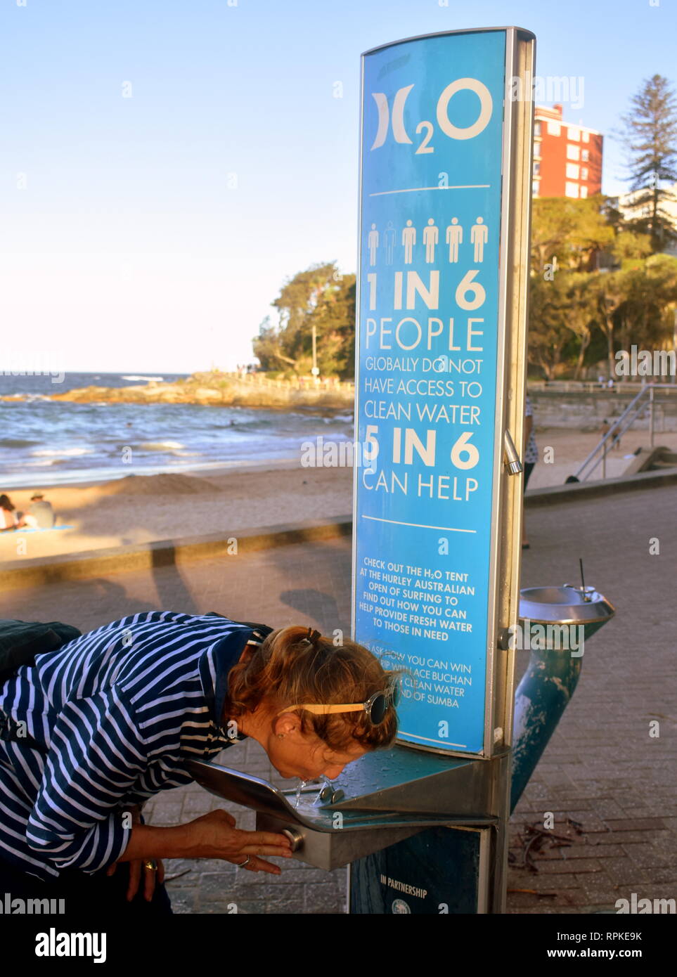 Lors d'une fontaine d'eau potable à Manly Beach, une femme prend un verre à côté d'un message environnemental sur le monde d'accéder à l'eau douce Banque D'Images