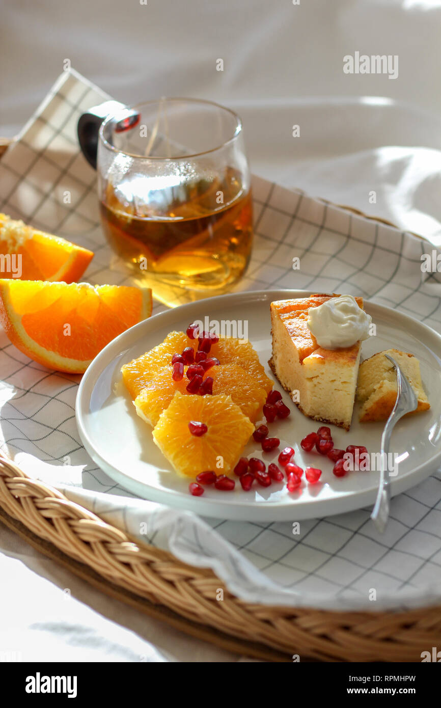 Matin dans le lit avec un morceau de gâteau et quelques tranches d'orange avec du thé sur un plateau Banque D'Images