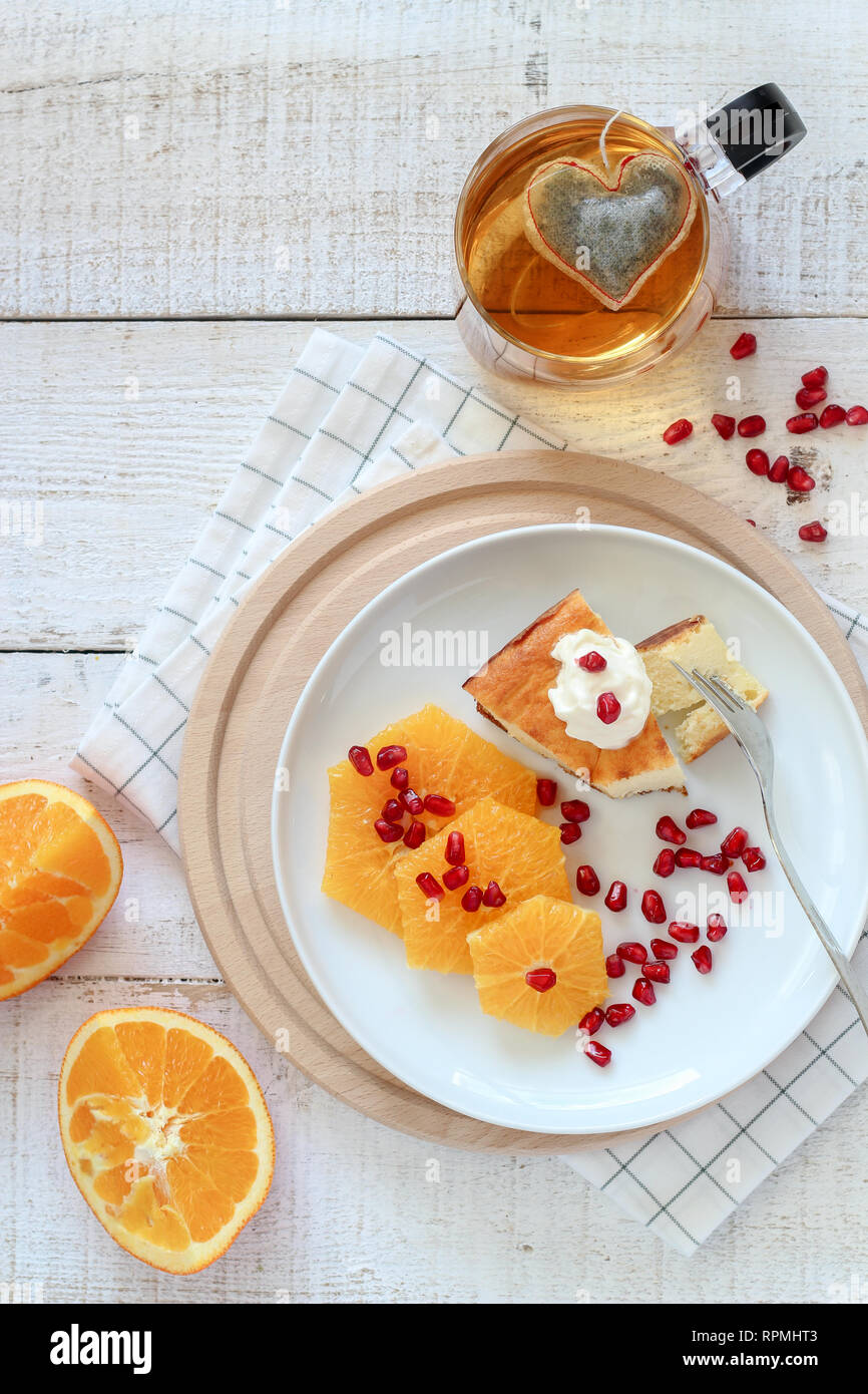 Petit-déjeuner télévision fixer la composition avec un morceau de gâteau, quelques tranches d'orange et une tasse de thé avec un sachet de thé en forme de coeur il Banque D'Images