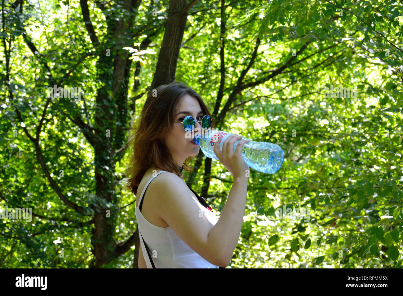 Une jeune femme boire d'une bouteille d'eau. Girl à lunettes rondes de l'eau potable dans les forêt Banque D'Images