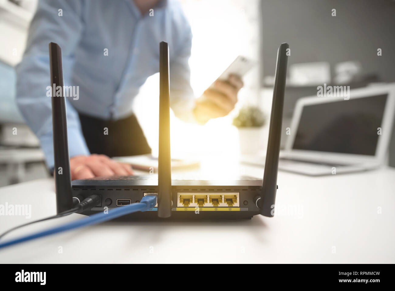 Routeur sans fil avec trois antennes et câble connecté. Man using smartphone en arrière-plan Banque D'Images