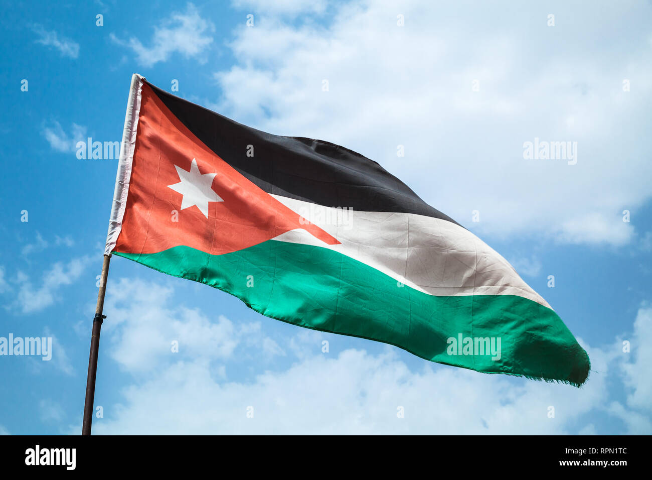 Brandissant le drapeau de la Jordanie sur le vent sur fond de ciel bleu nuageux Banque D'Images