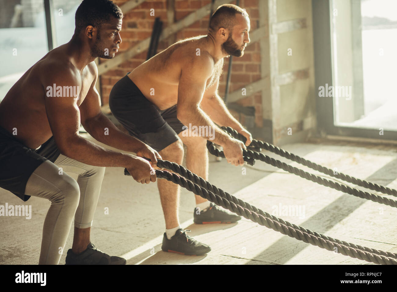 Deux hommes torse nu multiethnique bodybuilders sont l'exercice de combat avec des cordes. La haute intensité et la nature de la formation rapide avec un effet corde Banque D'Images