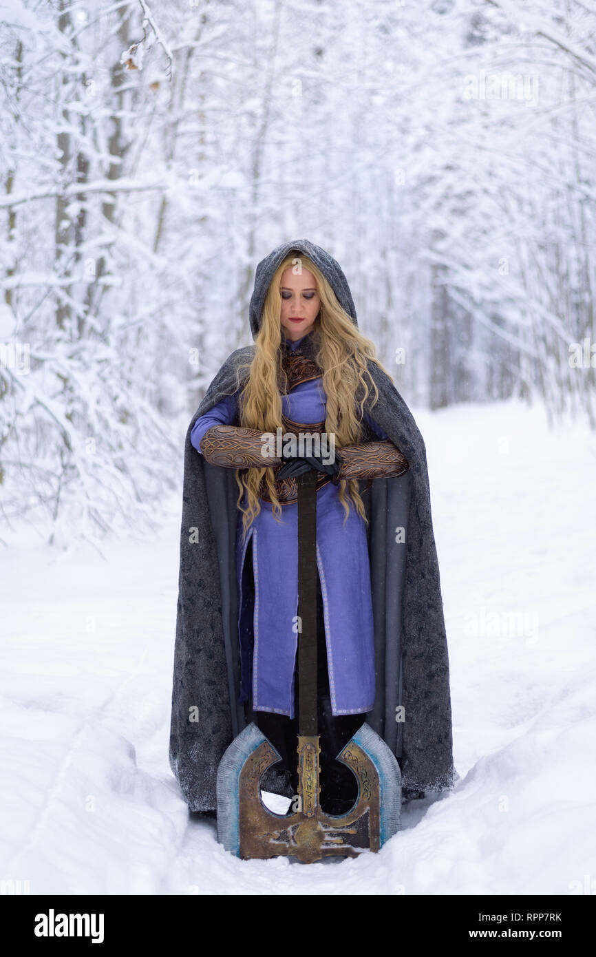 Warrior girl aux cheveux blonds et aux gros ax en forêt d'hiver Banque D'Images