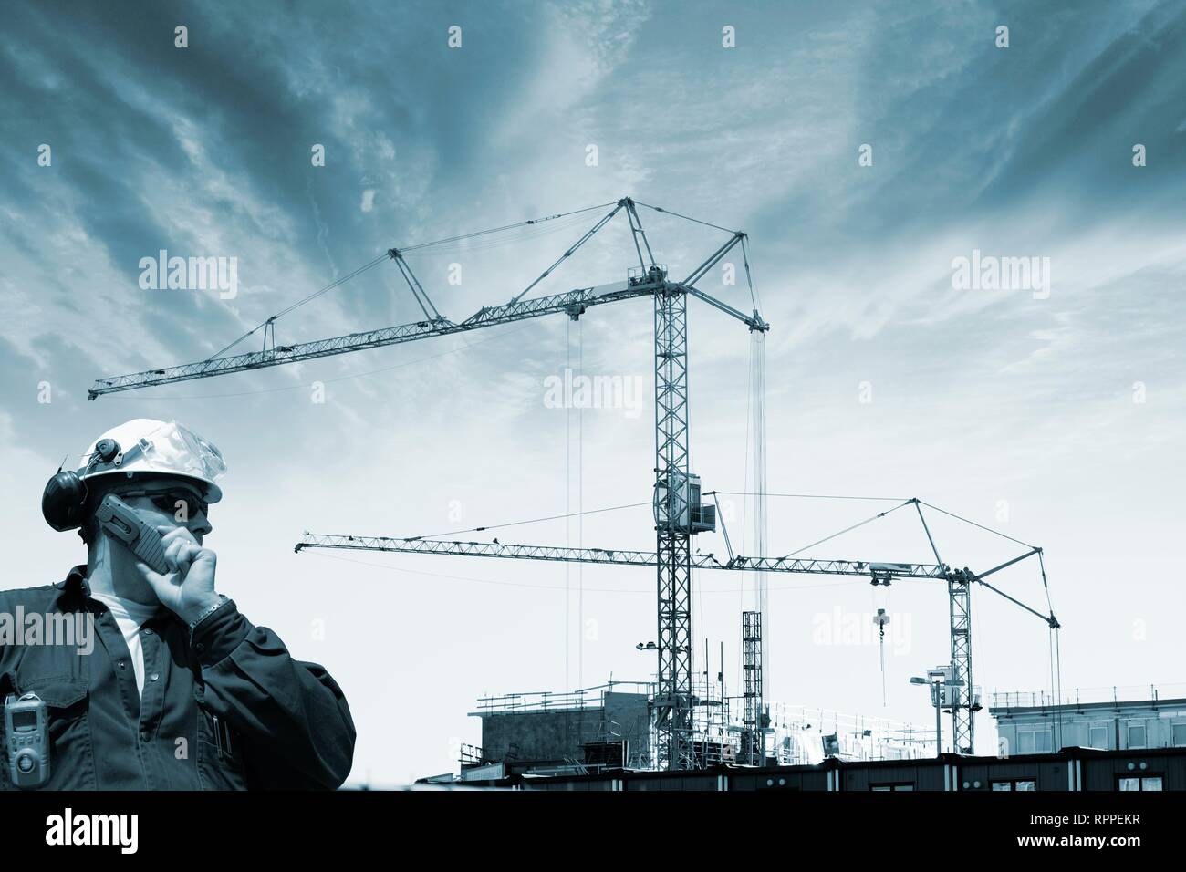 Construction Worker talking on mobile phone, avec des grues et des échafaudages en arrière-plan. Banque D'Images