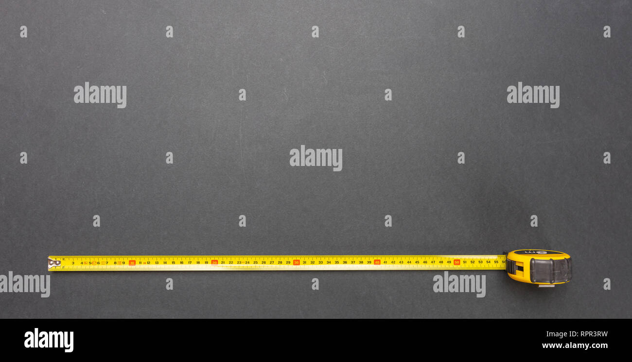 La mesure. Ruban mesure jaune isolé sur fond de couleur noire, vue du dessus, copy space Banque D'Images
