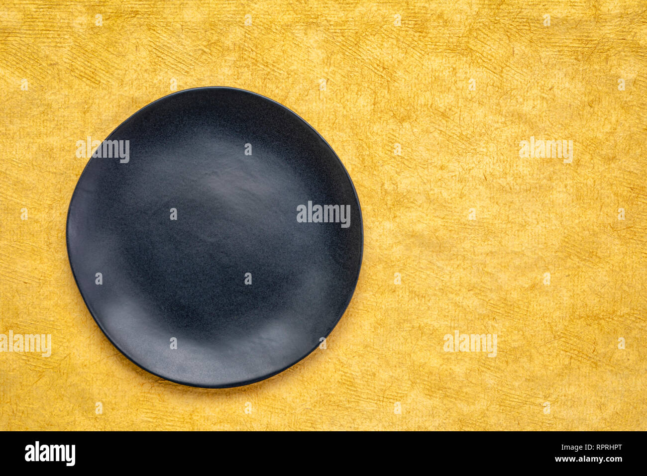 Plaque en céramique noire avec un bord irrégulier sur un papier fait main jaune Maya Huun avec une copy space Banque D'Images