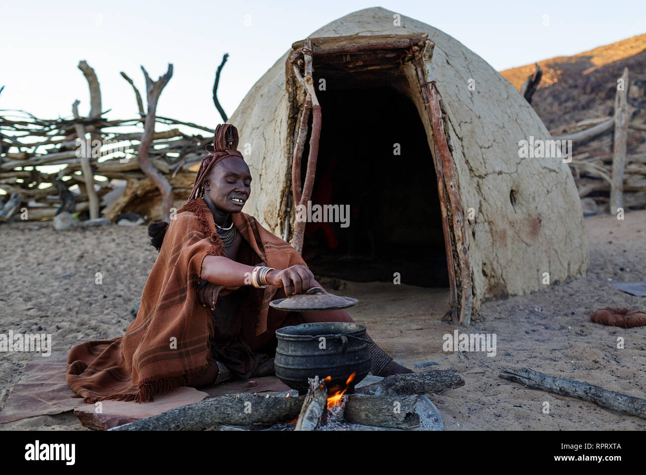 Femme Himba cuire le dîner sur le feu à l'extérieur de la cabane de torchis. Purros, Nambia, Afrique Banque D'Images