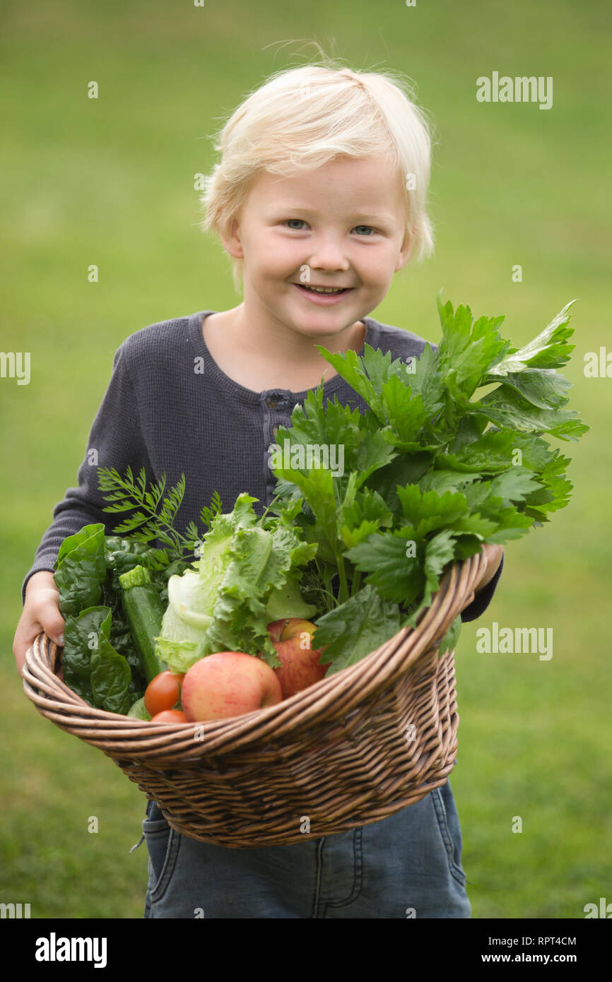 Un enfant blond heureusement montre sa récolte de fruits et légumes Banque D'Images