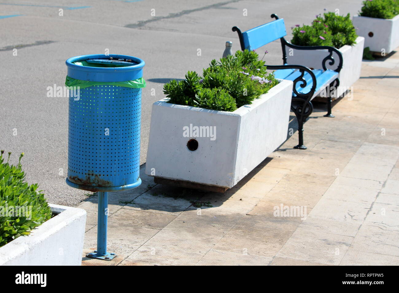 Blue metal poubelle publique avec nouveau sac en plastique dans la même  rangée banc public en bois bleu avec châssis de fer noir et blanc des pots  de fleurs en béton Photo