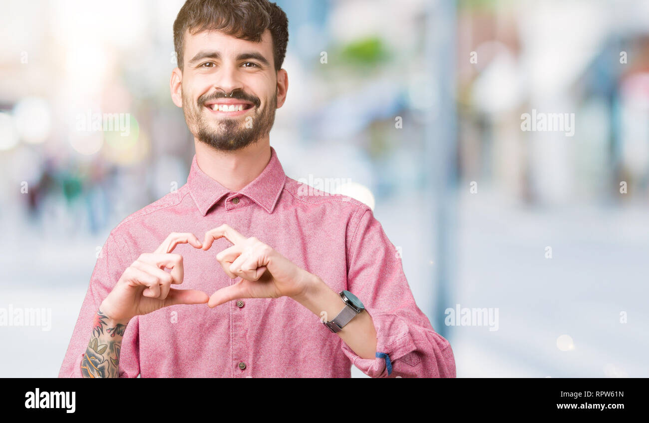 Beau jeune homme portant chemise rose sur fond isolé smiling in love montrant le symbole de coeur et la forme des mains. Concept romantique. Banque D'Images