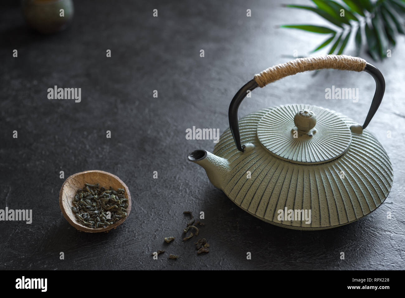 Théière et thé sur fond noir, copiez l'espace. Arrangement traditionnelle asiatique pour la cérémonie du Thé - Théière fer et sécher le thé vert. Banque D'Images