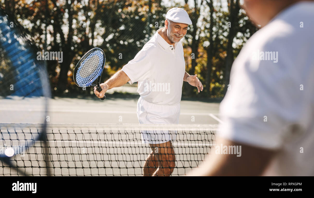 Cheerful senior hommes en faisant un match de tennis en plein air. Smiling senior man dans l'usure de tennis jouer au tennis avec un ami. Banque D'Images
