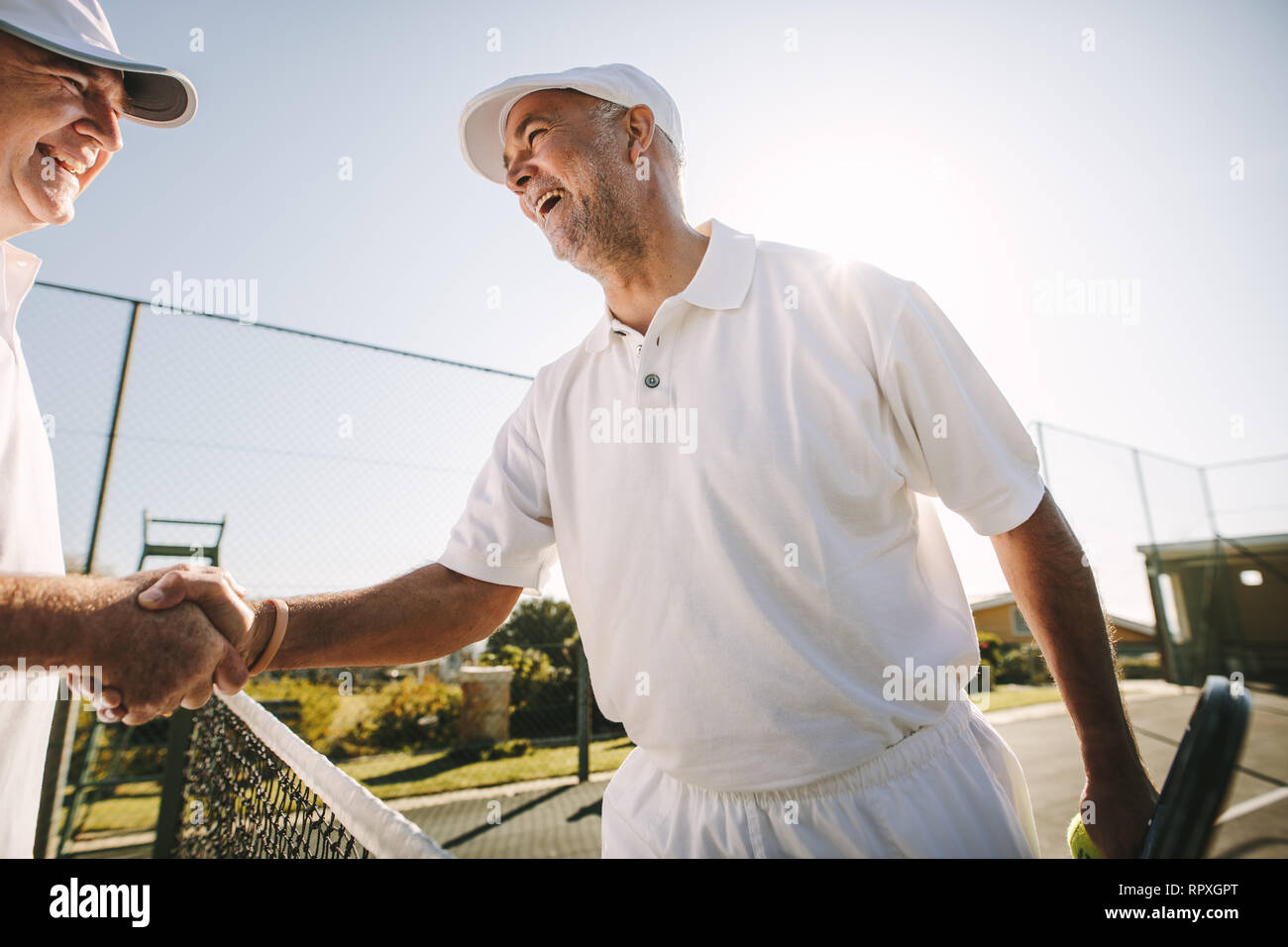 Deux cheerful senior les joueurs de tennis se serrer la main sur un court de tennis. Heureux les joueurs de tennis chaque message d'autres après une partie de tennis. Banque D'Images