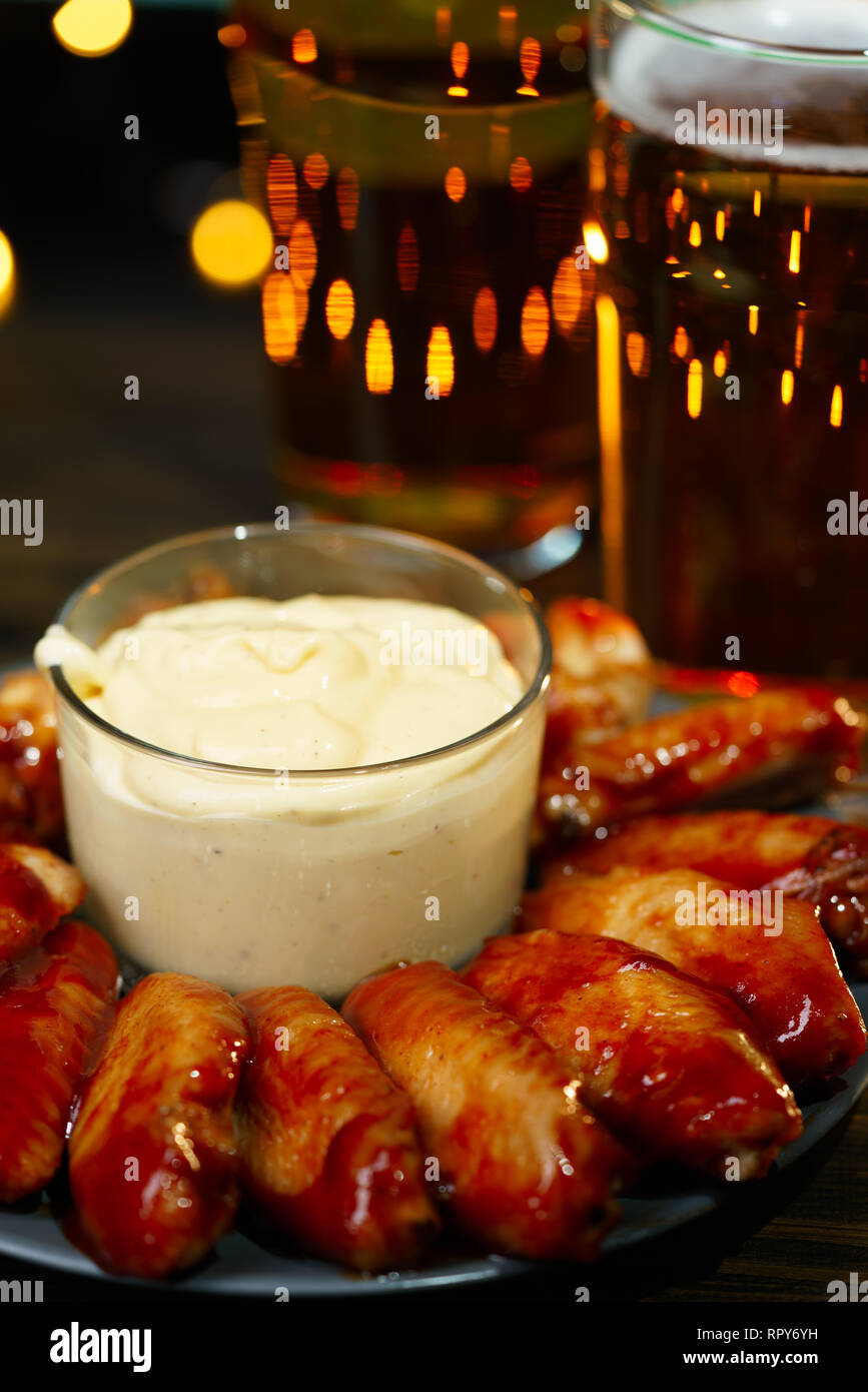 Ailes de poulet barbecue chaud avec 2 verres de bière sur une table en bois foncé servi avec sauce miel moutarde. Lumières de fête sur un arrière-plan, la haute résolution Banque D'Images