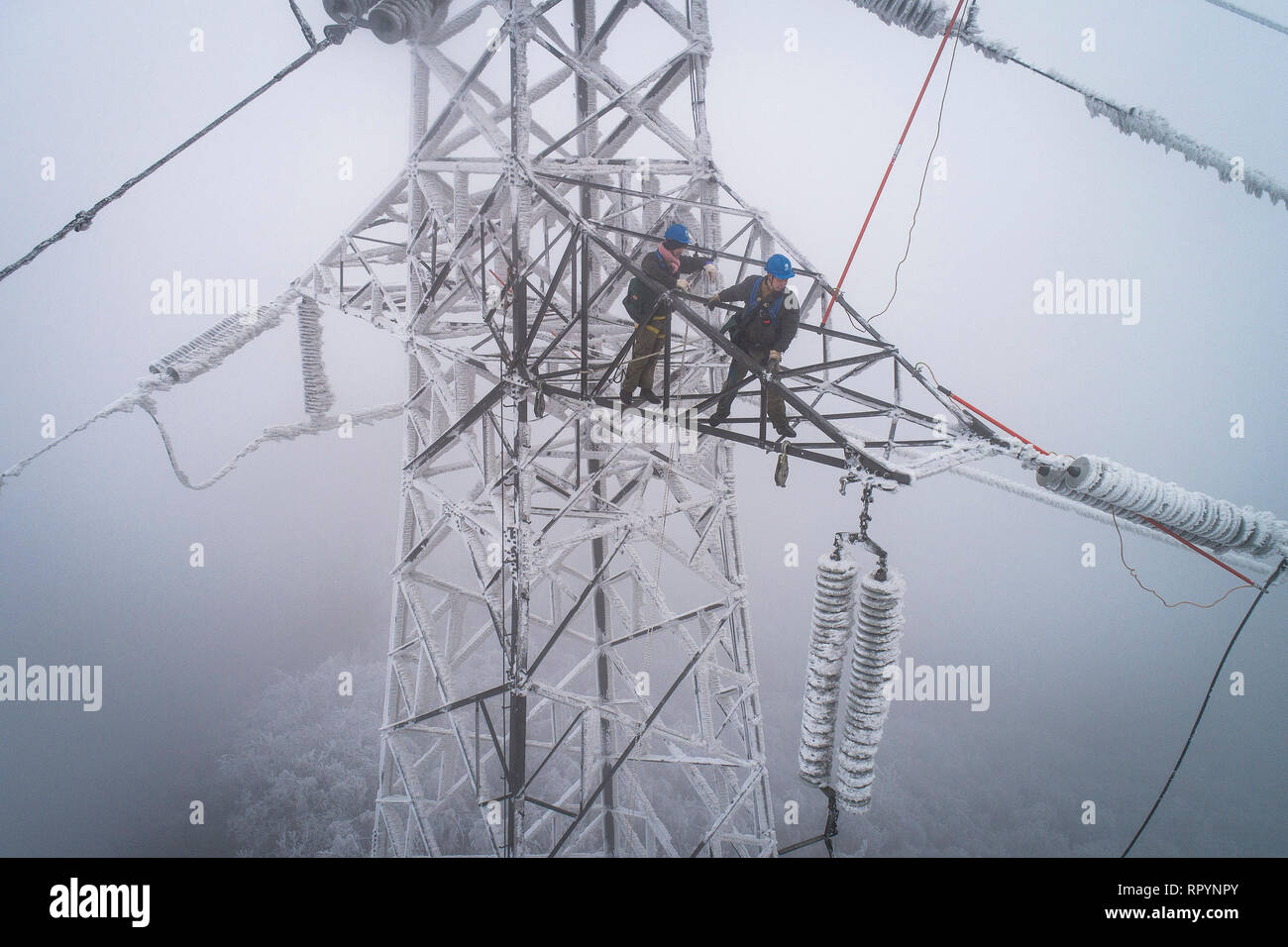 (190223) -- Wuhan, 23 février 2019 (Xinhua) -- photo aérienne prise le 12 février 2019 montre d'urgence Dong Jinbing (L) de l'inspection du fil haute tension avec son collègue Wang Wensheng sur la tour de transmission de puissance dans la zone de montagne de Wuhan, capitale de la province du Hubei en Chine centrale. Une équipe d'électriciens a été envoyé pour réparer un fil haute tension qui a été rompu en raison de l'épaisse couche de l'accumulation de glace. Après une journée de travail sur le plus de 40 mètres de haut de la tour de transmission de puissance de mauvaise condition météorologique, l'équipe réussi à fixer la défaillance de l'alimentation système qui réduit la vitesse des trains ca Banque D'Images