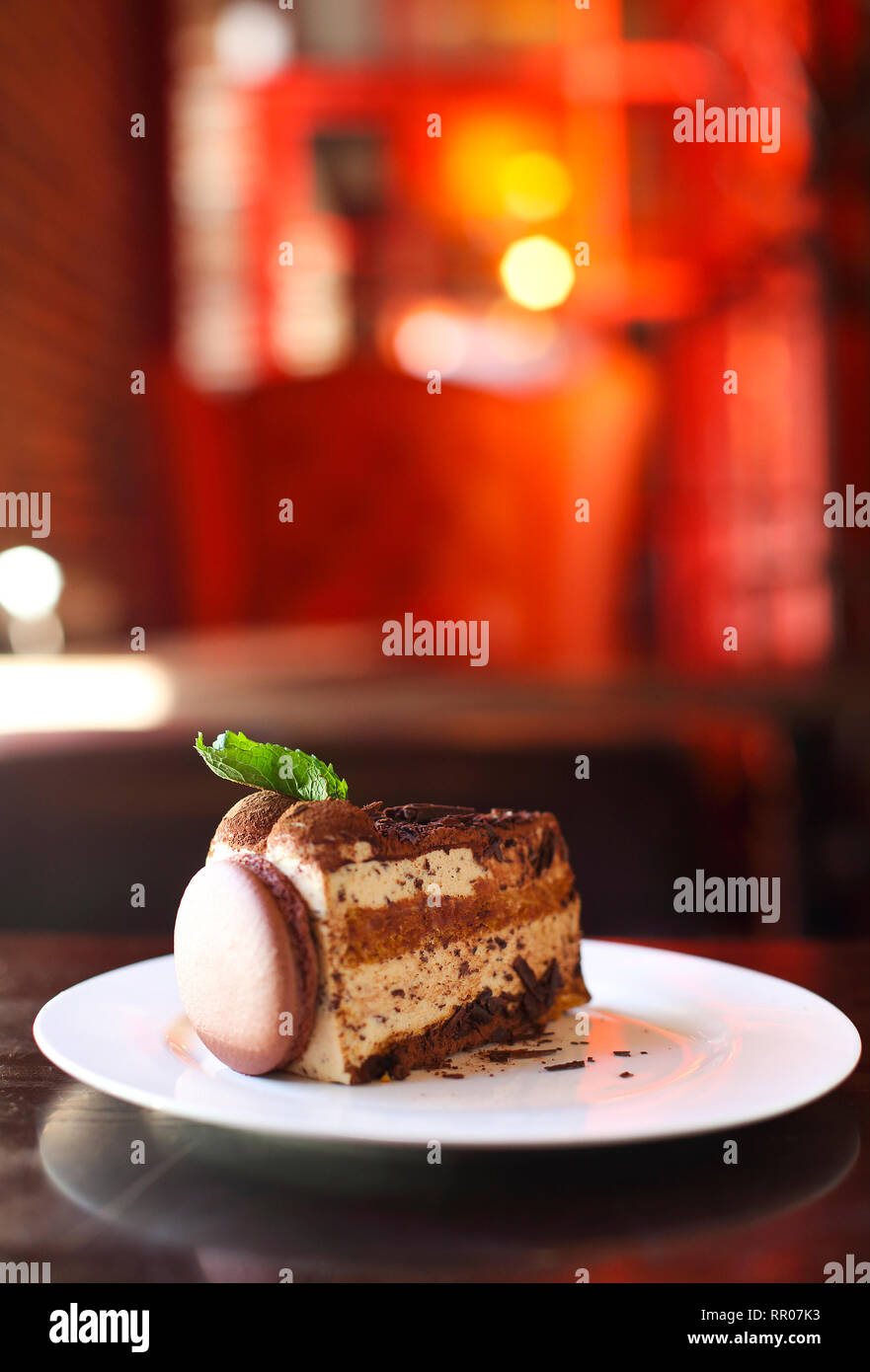 Morceau de gâteau au chocolat décoré de macaron et de menthe sur plaque blanche, selective focus, arrière-plan lumineux Banque D'Images