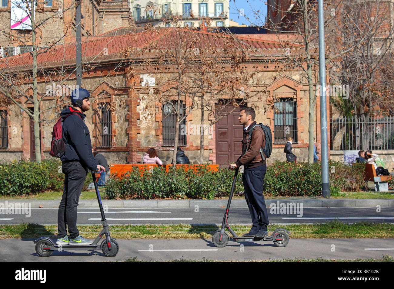 Scène de deux hommes à cheval des scooters électriques ('e-scooter) à Barcelone, Espagne. Banque D'Images