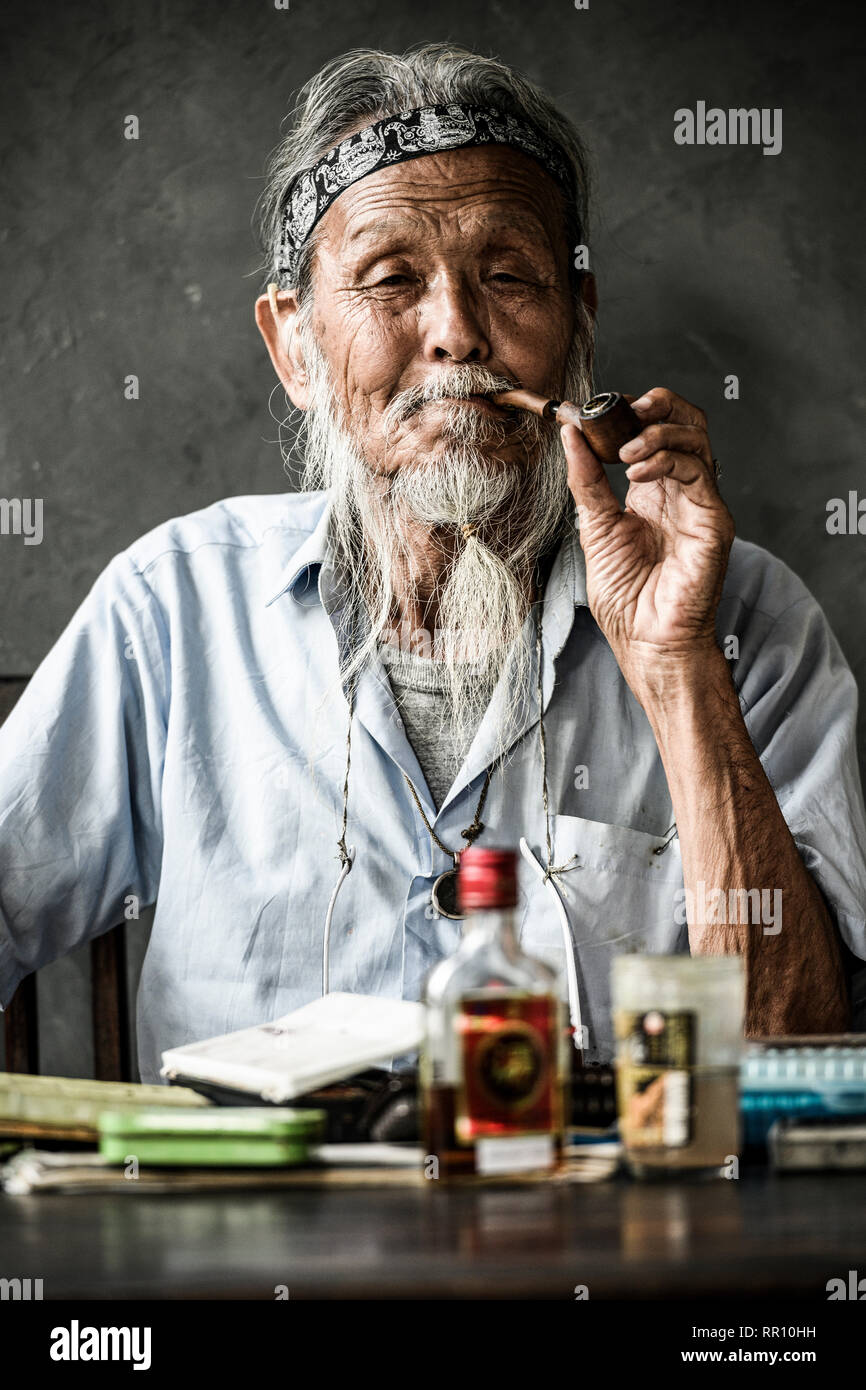 Portrait d'un vieil homme japonais fumant une pipe tandis que sur la table il y a une bouteille de rhum et de peinture. Osaka, Japon. Banque D'Images