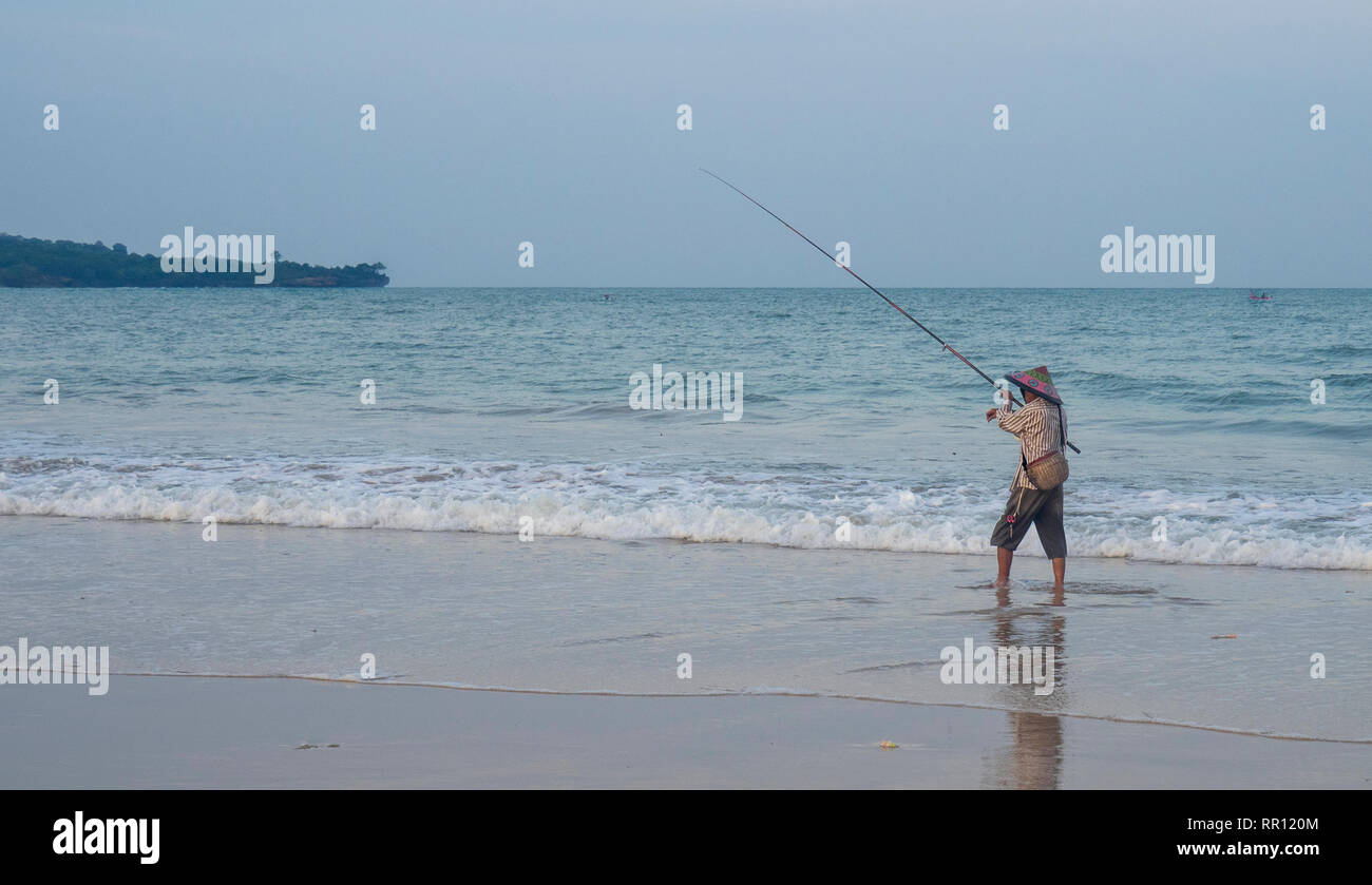 Pêcheur solitaire portant un chapeau conique à l'aide d'une canne de pêche au large de la plage de La Baie de Jimbaran Bali Indonésie. Banque D'Images