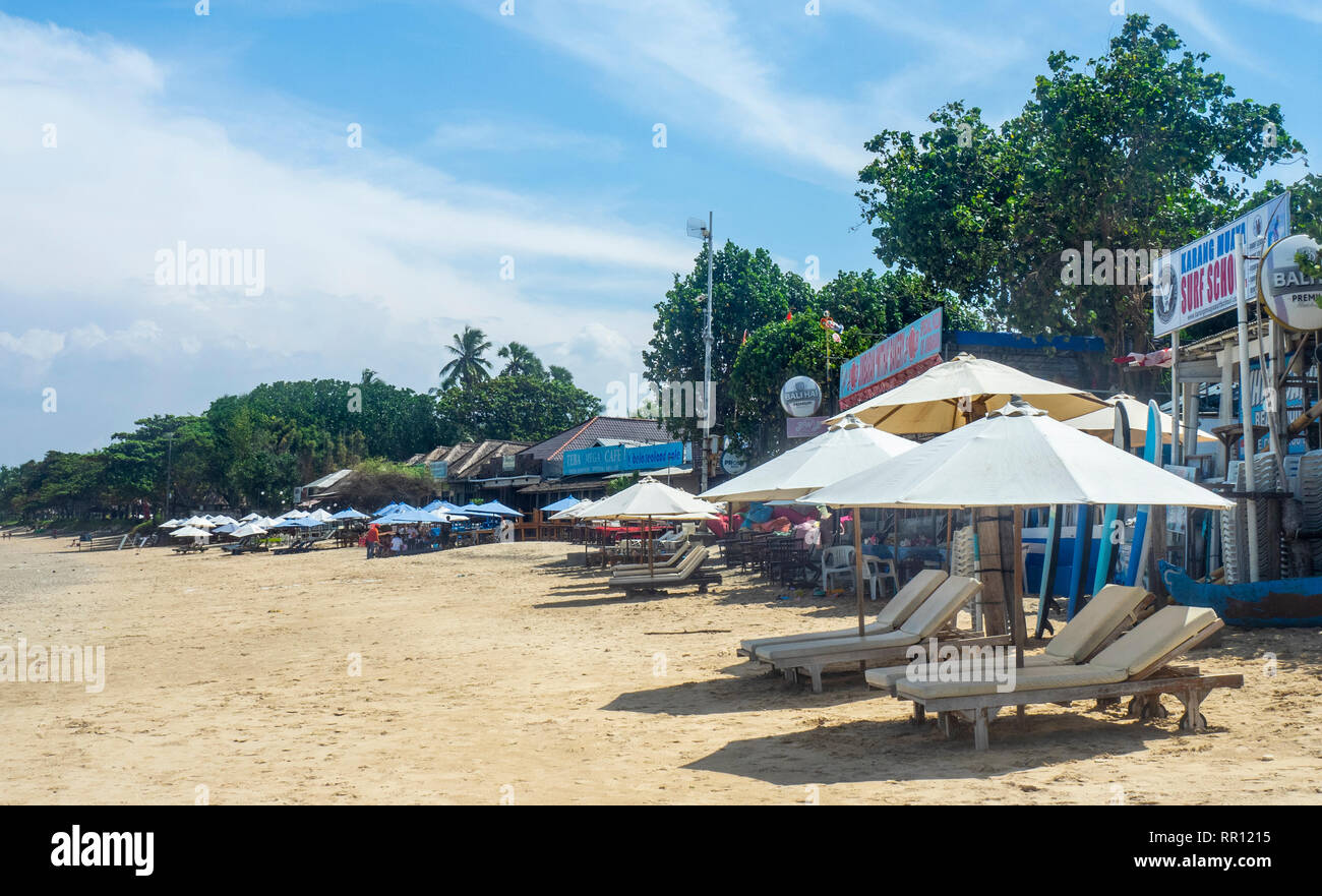 Des chaises longues et des parasols sur la plage en face d'une rangée de restaurants de fruits de mer de la Baie de Jimbaran Bali Indonésie. Banque D'Images