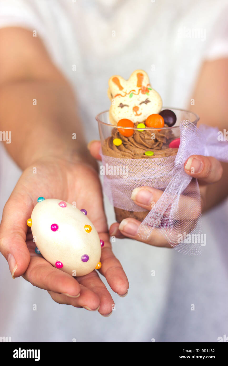 Woman's hands holding tasse en plastique transparent avec la mousse au chocolat dans une main et décoré oeuf de Pâques dans l'autre Banque D'Images