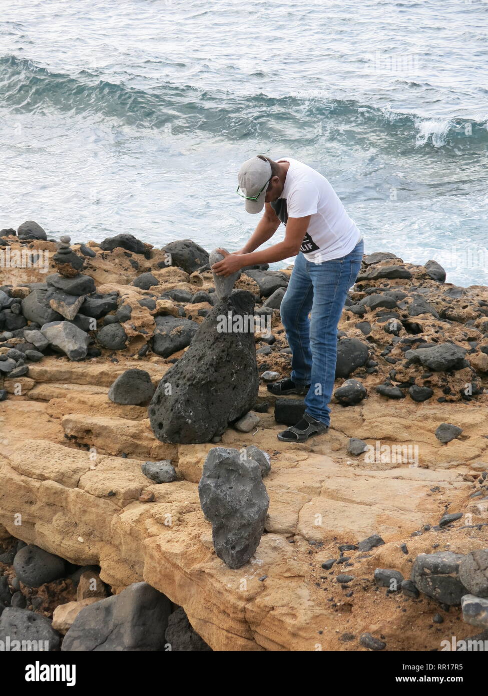 L'homme sur la mer à Playa Blanca créer rock art statues en équilibrant les pierres : créativité artistique ou la destruction de l'écosystème ? Banque D'Images