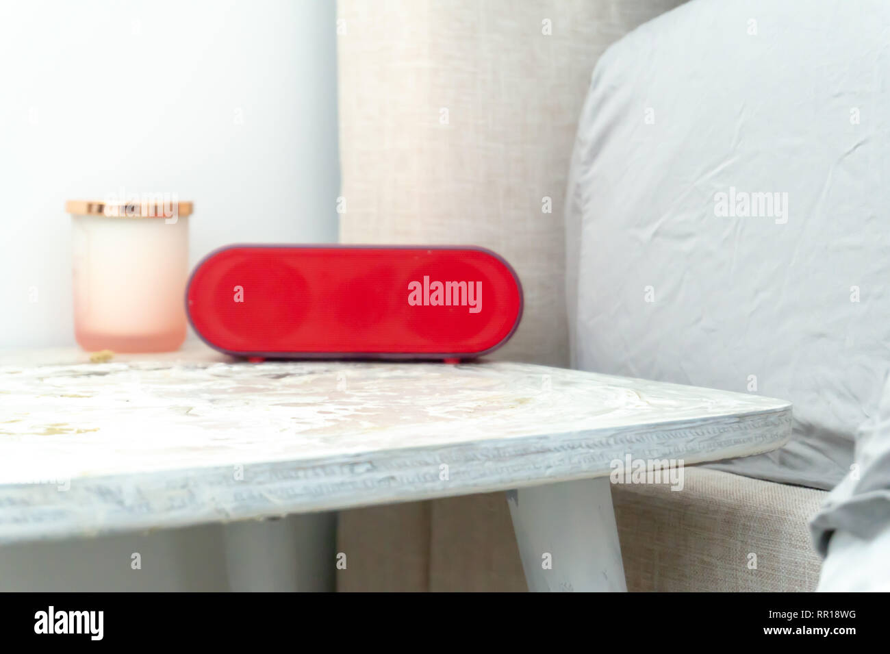Radio réveil rouge vif et photophore sur une table de chevet table de nuit, avec linge de lit et montrant dans des tons doux. Banque D'Images
