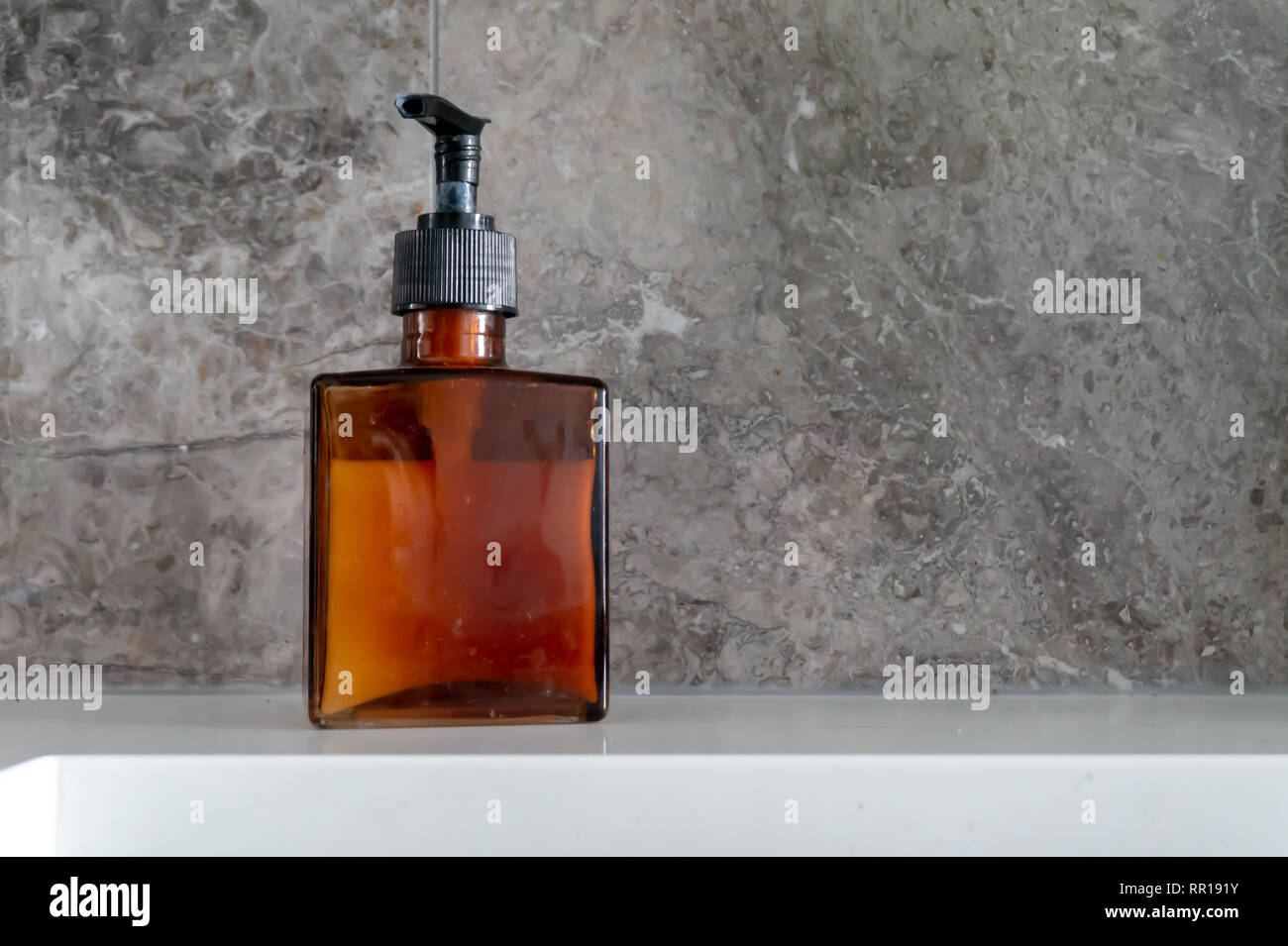 Distributeur de savon à main dans une bouteille de verre brun, carré, avec pompe noir et gris en dosseret près de l'évier de la cuisine. Illustrant les mains propres, lavage. Banque D'Images