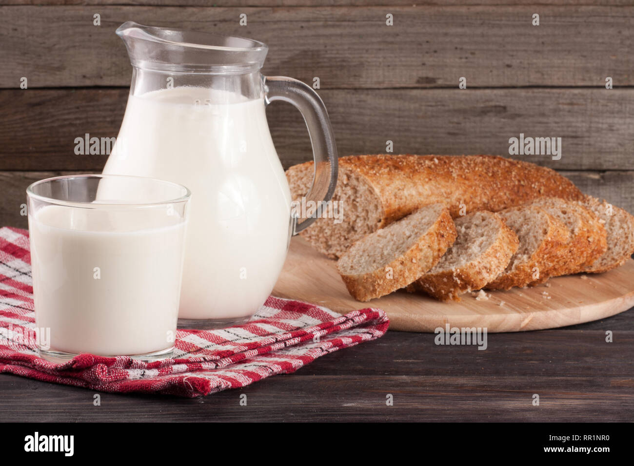Verseuse et verre de lait avec une miche de pain sur un fond de bois Banque D'Images