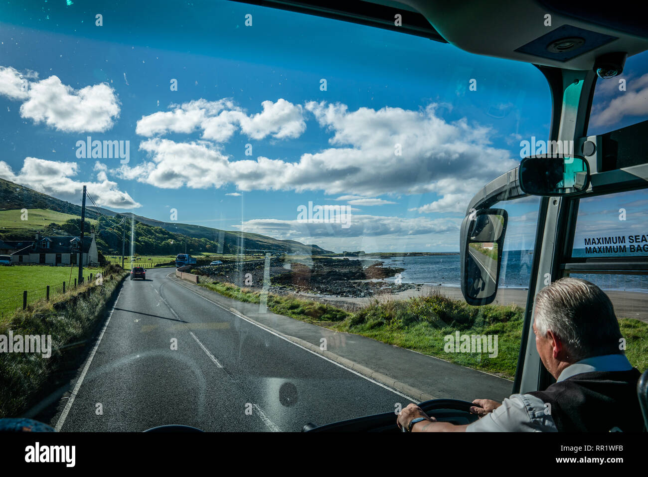 En regardant par la fenêtre avant d'un autobus. Voir le conducteur de l'autobus et la campagne de l'Ecosse. Des champs verts et des deux côtés de l'océan. Banque D'Images