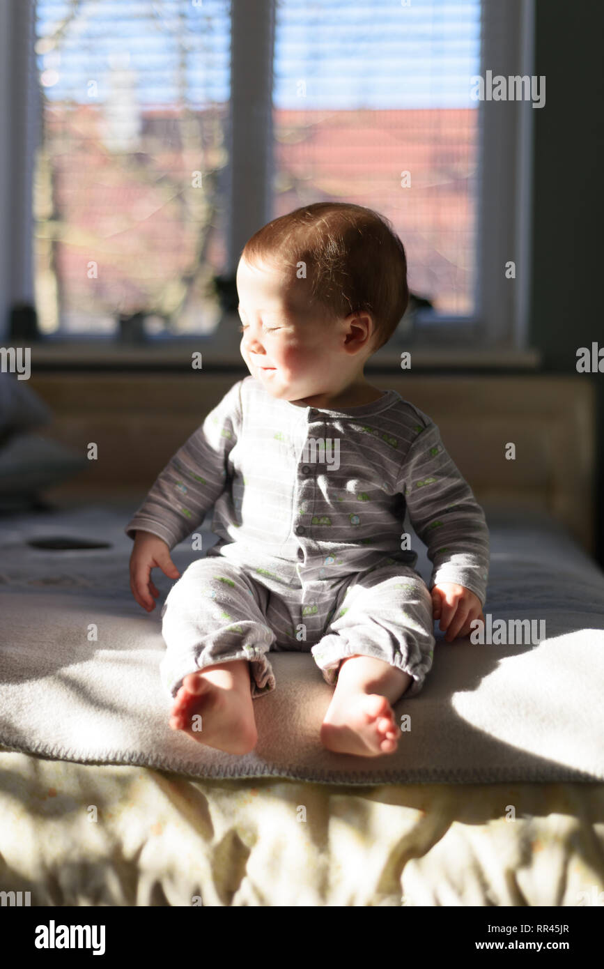 Happy Baby Boy en pyjama gris sur lit dans sa chambre Banque D'Images