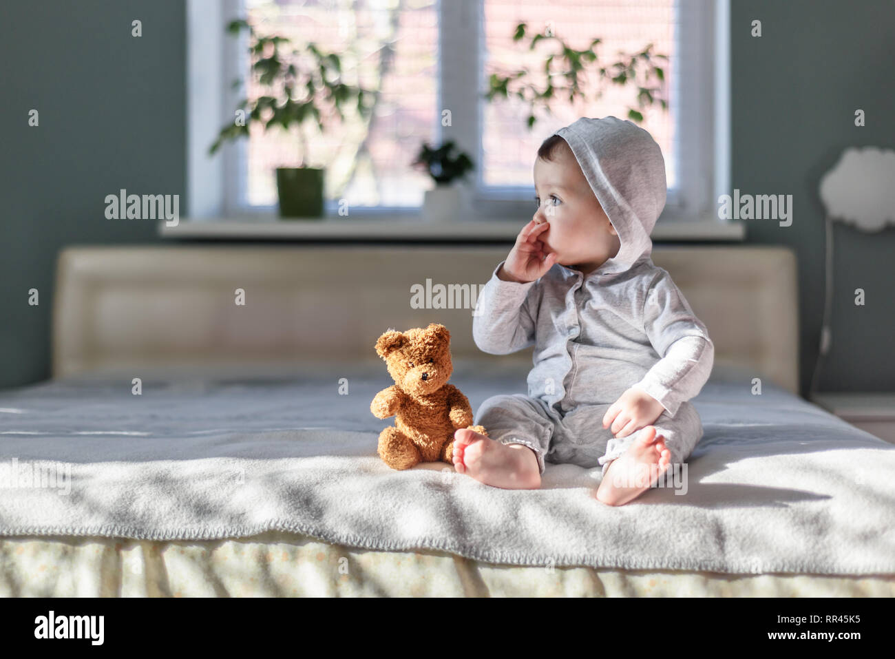 Happy Baby Boy en pyjama gris sur lit dans sa chambre Banque D'Images