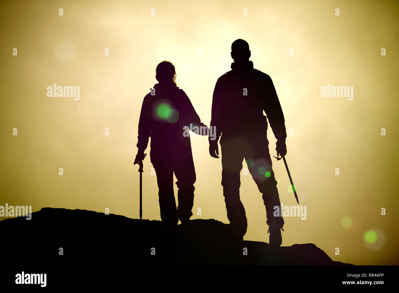 Couple de rétroéclairage des alpinistes avec cannes de marche au coucher du soleil Banque D'Images