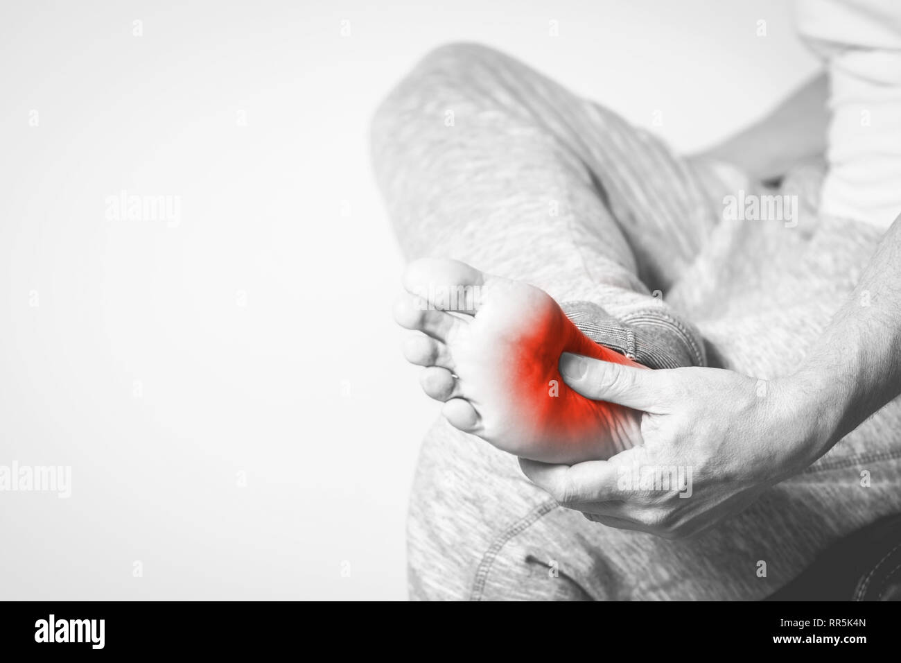 Homme Causian détient les mains pour ses pieds douloureux, des douleurs à pied. La photographie en noir et blanc. Couleur rouge est domaine de la douleur Banque D'Images