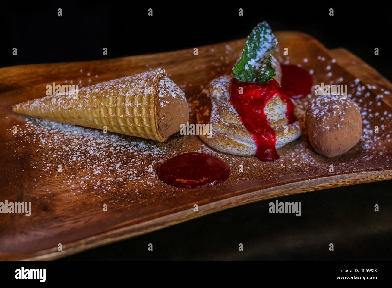 Cornet de crème glacée servie sur un plateau en bois avec de la crème chantilly, de la confiture et une feuille de menthe, saupoudrée de poudre de cacao et de sucre en poudre Banque D'Images