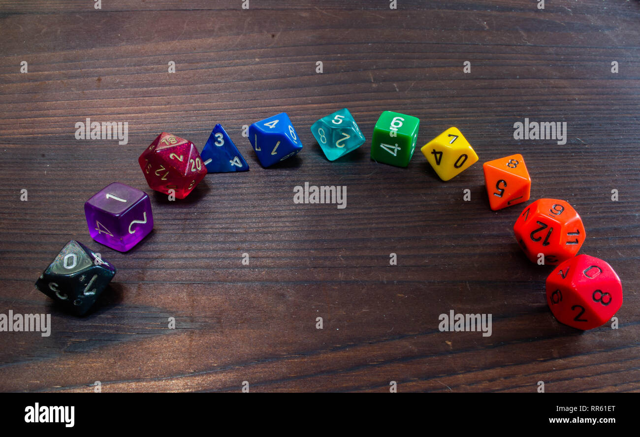 Divers types de plastique coloré jeu dés polyédriques disposées en un arc-en-ciel sur une table en bois Banque D'Images