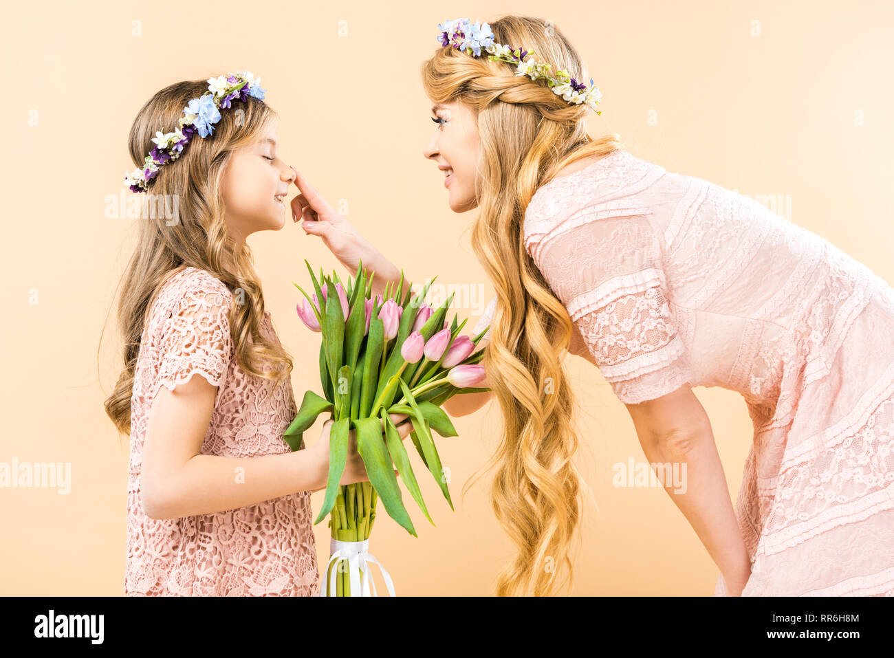 Cute Child holding bouquet de tulipes roses avec les yeux fermés tout en touchant son nez mère joyeuse sur fond jaune Banque D'Images