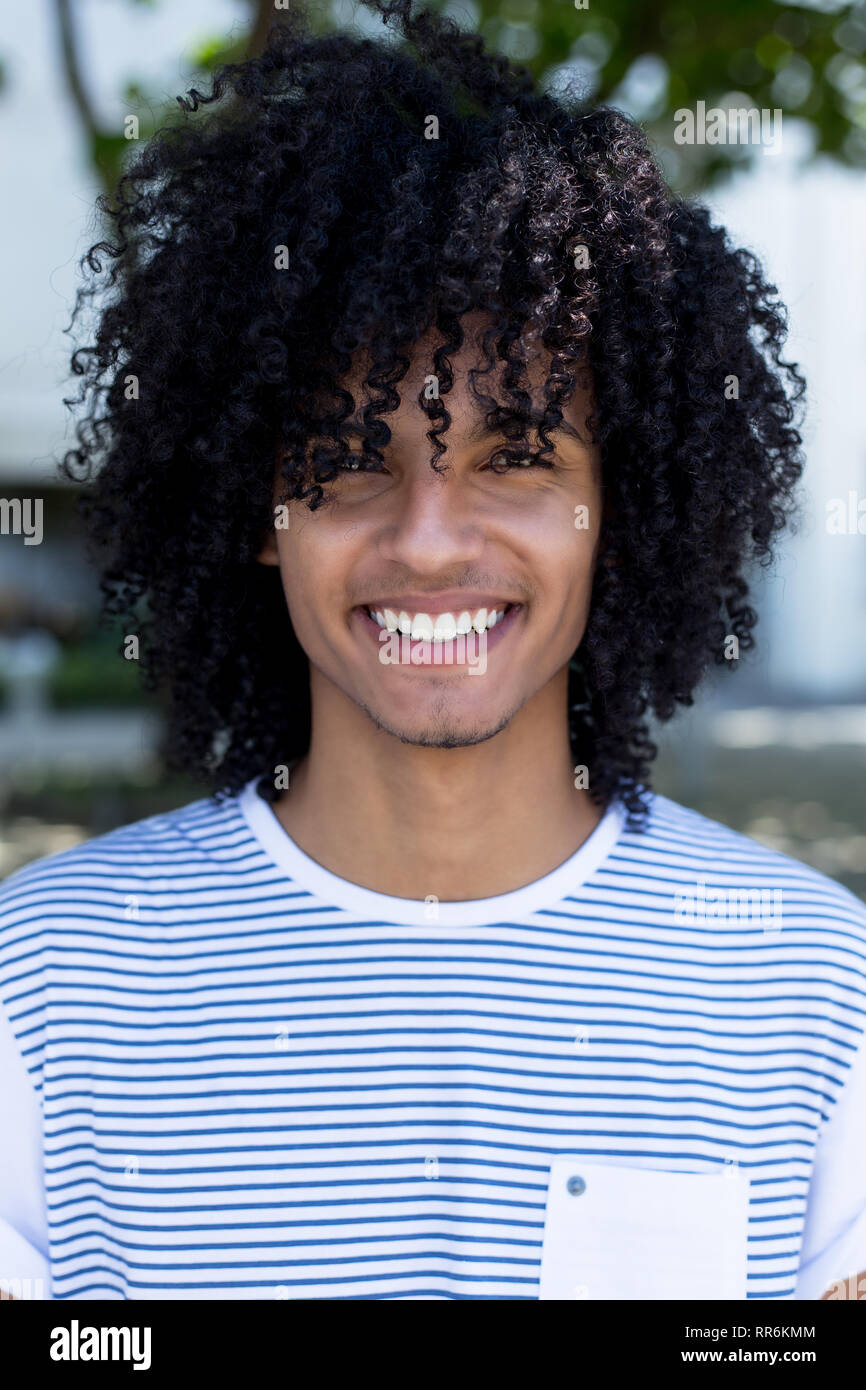 Portrait of laughing young adult man latino-américain avec de longs cheveux bouclés dans la ville en plein air Banque D'Images