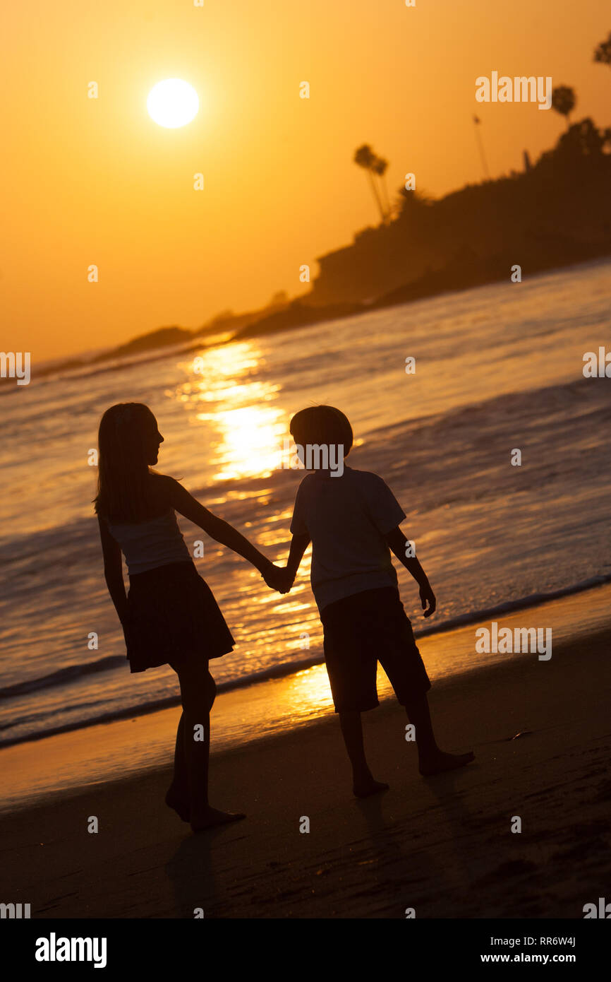 La silhouette d'une fratrie marche main dans la main le long du rivage de Laguna Beach, en Californie. Banque D'Images