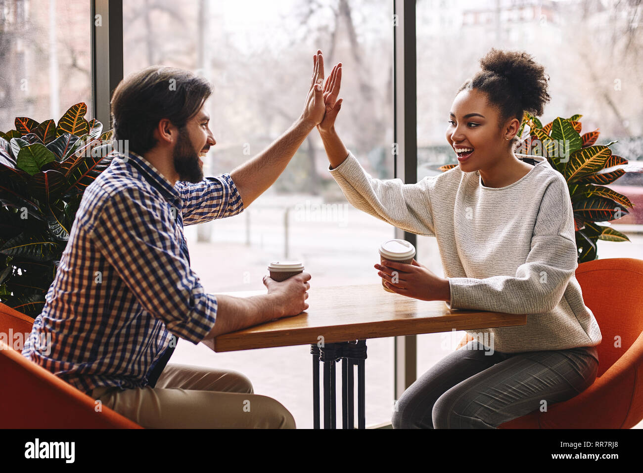 Heureux les jeunes entrepreneurs dans les tenues à cafe table ou bureau d'affaires en offrant un rapport de cinq à l'autre comme s'Célébrons les succès ou de commencer un nouveau projet. African American Woman and Caucasian brun Banque D'Images