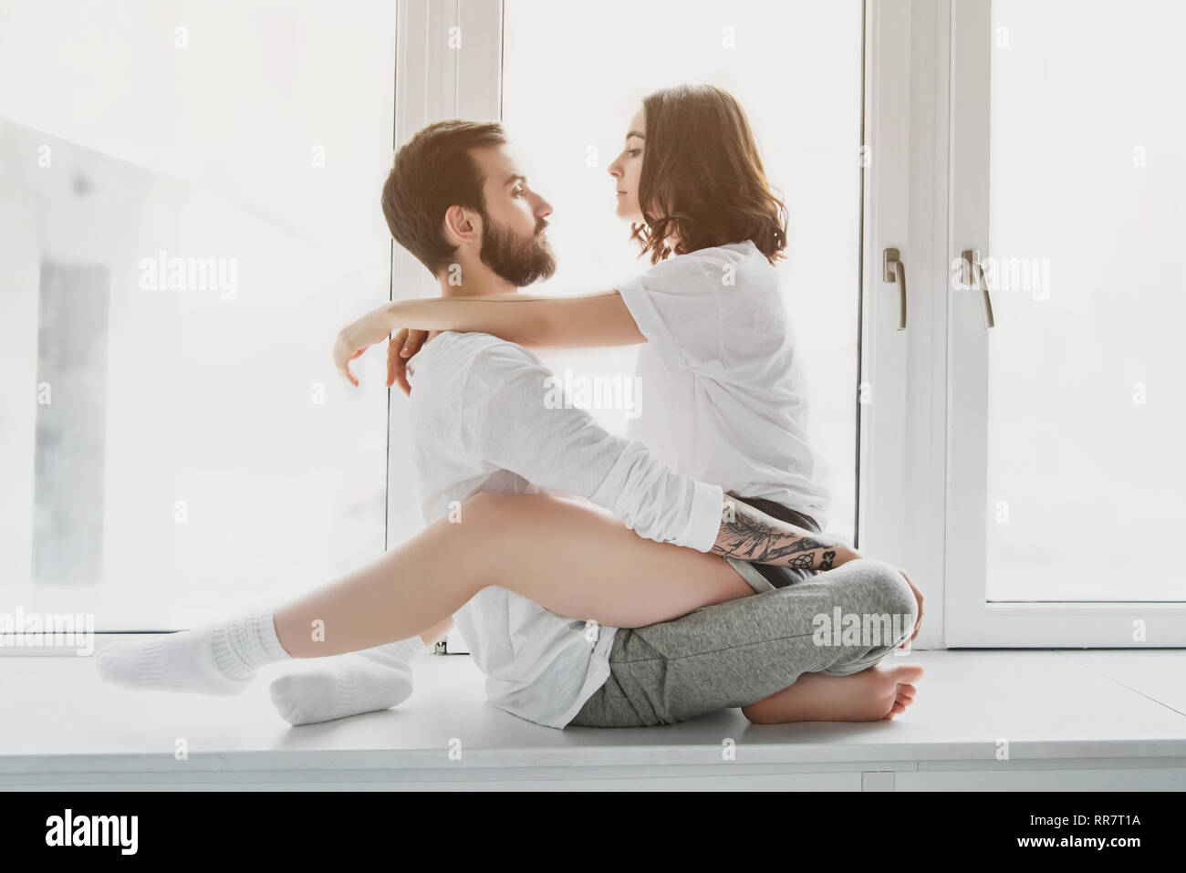 Beau jeune couple, serrant et assis sur un rebord de fenêtre à la maison Banque D'Images