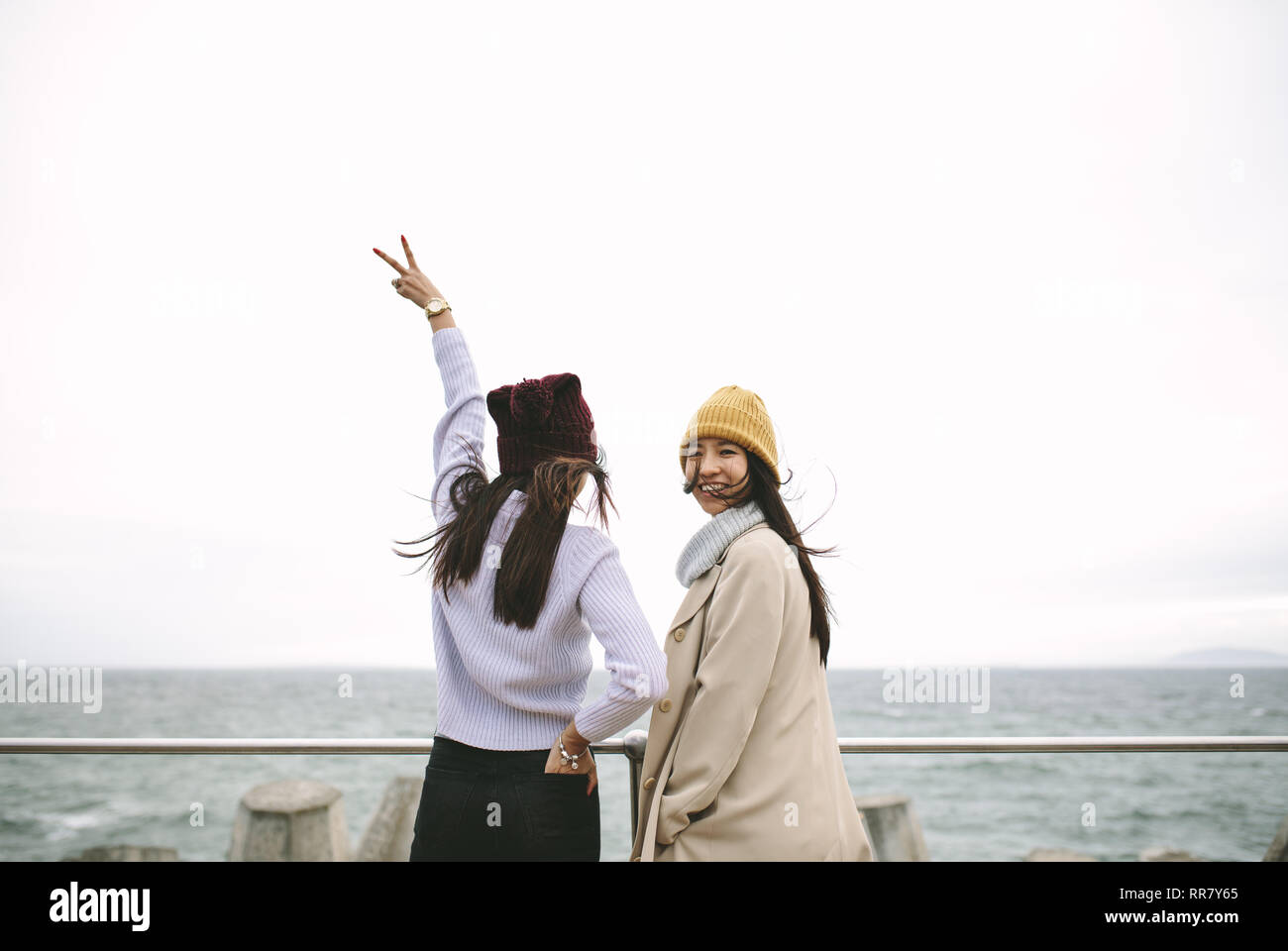 Vue arrière d'une femme debout près de la mer avec la main posée montrant la victoire. Girl friends admirant la vue sur la mer par une froide matinée d'hiver. Banque D'Images