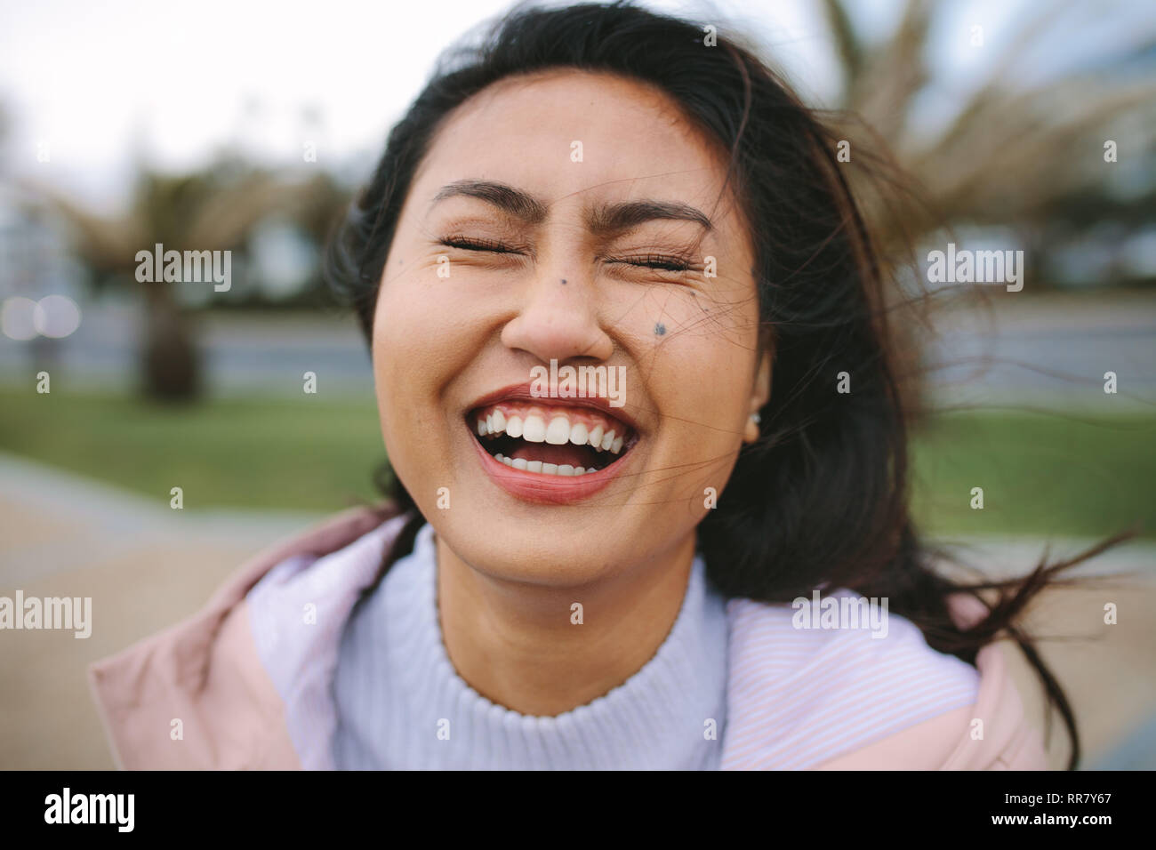 Portrait of a woman standing outdoors et rire. Close up d'une femme asiatique rire avec les yeux fermés. Banque D'Images