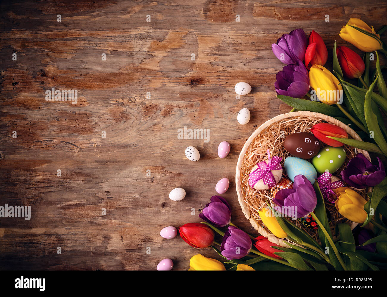 Oeufs de Pâques dans un panier avec des tulipes sur fond de bois vieux Banque D'Images