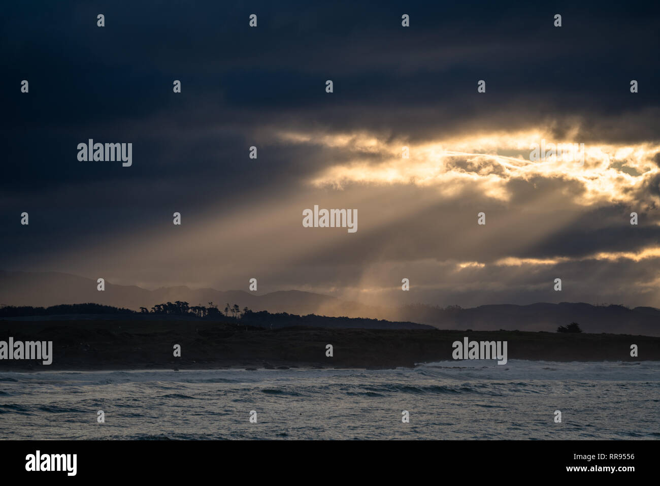 Lever tôt le matin avec les rayons de lumière en streaming à partir d'une ouverture dans les nuages, illuminant le littoral près de Cambria, San Simeon, en Californie. Banque D'Images
