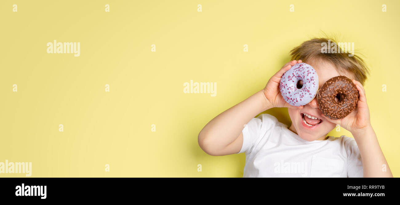 Boy holding donuts par ces yeux, arrière-plan lumineux Banque D'Images