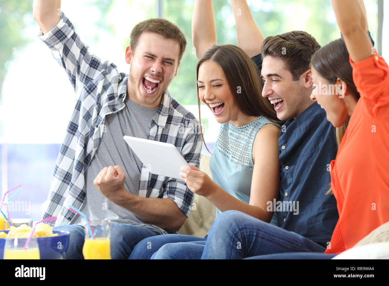 Groupe d'amis excités regardant médias sur tablet assis sur un canapé dans la salle de séjour à la maison Banque D'Images